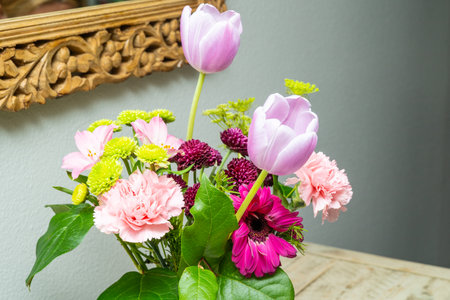 A vibrant bouquet of tulips, carnations, and chrysanthemums creates a striking floral still life against a textured background.の写真素材