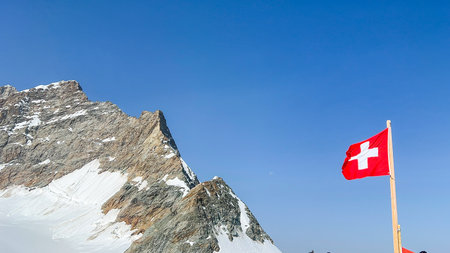 A view of the Jungfraujoch in Switzerland with the Swiss flag waving in the wind on a clear day.