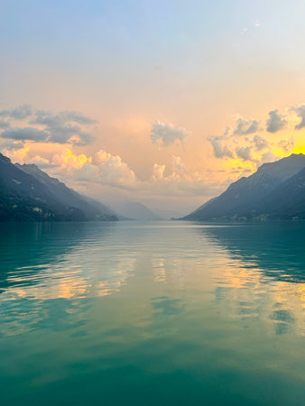 Calm waters of Lake Brienz in Switzerland reflect the colorful sunset sky and surrounding mountains. A serene landscape capturing the beauty of the Swiss Alps.の写真素材
