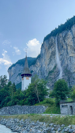 Picturesque view of Lauterbrunnen Church and Staubbach Waterfall in the Swiss Alps, Switzerland. A stunning landscape with a beautiful waterfall cascading down a mountain.の写真素材