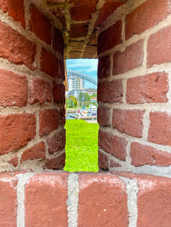 A glimpse of KoÅobrzeg Marina through the brick lookout. Lush green grass, boats, and the iconic bridge in the background.の写真素材