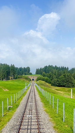 A captivating view of railway tracks heading towards a tunnel in Stoos, Switzerland, surrounded by green meadows and a lush forest.の写真素材