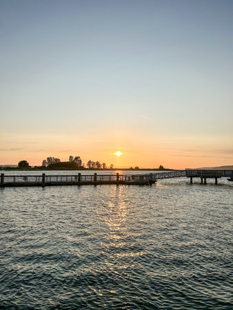 Golden hour paints a picturesque scene at a pier on Puget Sound. Reflections dance on the water as the sun dips below the horizon. Tranquil beauty.の写真素材