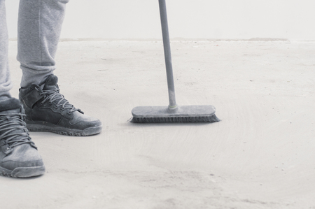 People, housework, cleaning and housekeeping concept - close up of legs with broom sweeping floor at...