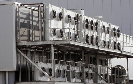 Several large air conditioners on the gray wall of an industrial plant