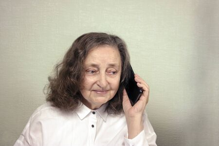 A beautiful elderly woman about 65 years old is happy, smiling, talking on a cell phone