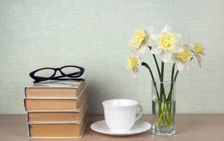 Daffodils, a white cup and saucer, books with glasses. Concept reading, classic literature. Place for text, copy spaceの写真素材
