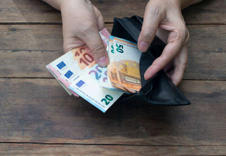 Hands put banknotes 10, 20, 50 euros in a black wallet on   woodenの写真素材
