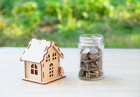 A small wooden house and a glass jar with coins. The concept of buying, selling, renting real estate, mortgage. Place for your text. Copspaceの写真素材