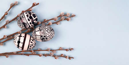 Easter eggs with black and white ornament among pussy willow branches on a blue background. Place...