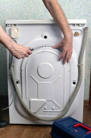 Washing machine repair. A man screws the back of a washing machine with a screwdriver. Repair of large household appliancesの写真素材
