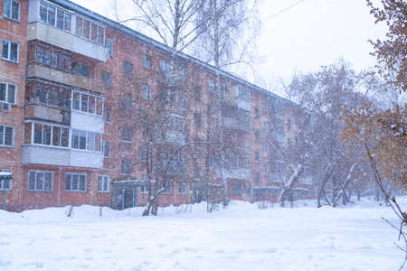 Snowy winter day. There are snowdrifts and trees without leaves in the courtyard of a five-story buildingの写真素材