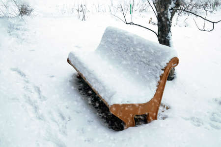 It's winter, it's snowing. The park bench is covered with snowの写真素材