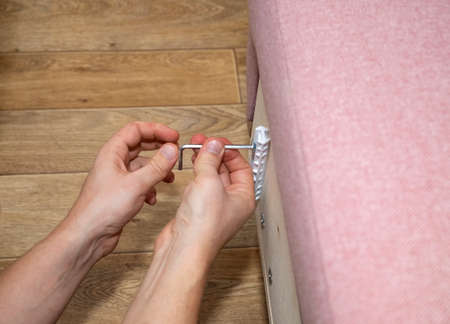 Furniture assembly. Male hands screw the mount to the side of the pink sofa