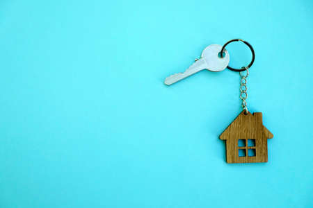 Key with a keychain in the form of a house on a blue background. The concept of buying, selling,...