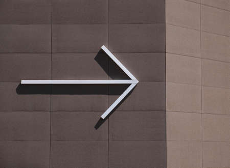 White arrow on the brown wall of the house in a sunny house