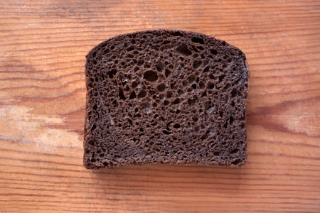 A piece of black rye bread lies on an old wooden board. food crisis conceptの写真素材