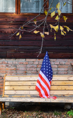 The American flag stands on the left side of the brick house. America, autumn leaves on the tree. vertical photoの写真素材