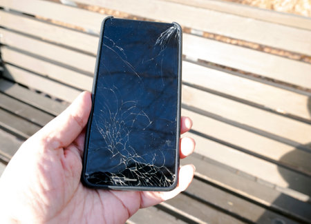 Broken smartphone in hands on a sunny day. Cracked mobile phone screen