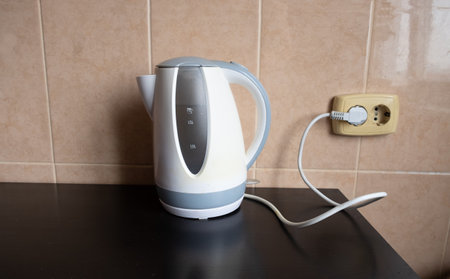 An electric kettle with water stands on the table in the kitchen, plugged into the socketの写真素材