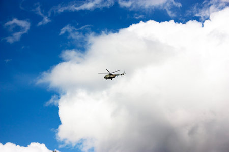 The helicopter flies against the background of a blue sky with cloudsの写真素材
