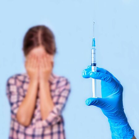 Hand in medical glove holds a syringe and the child is afraid of pricking with his eyesの写真素材