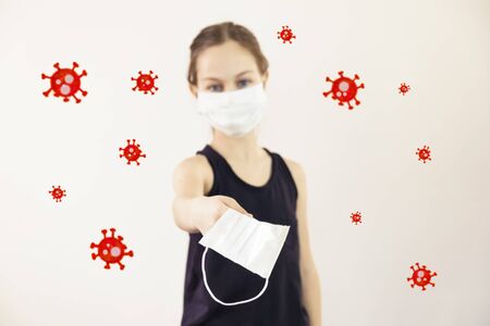 Teenage girl in a medical mask offers a medical mask to another around viruses flyの写真素材