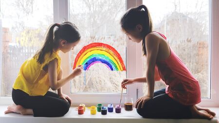 Two girls paint a rainbow on a window squattingの写真素材