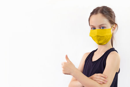 Teenage girl in a protective mask holds her hand with a raised thumb upの写真素材