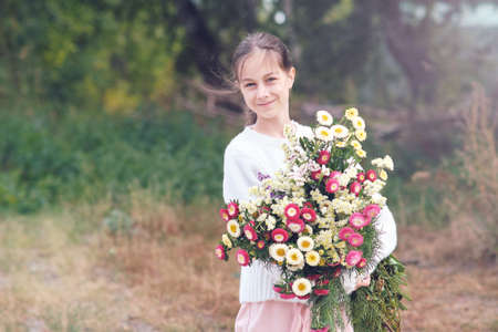 A girl holds in her hands a large beautiful bouquet of autumn flowers in a white sweater in a forest gladeの写真素材