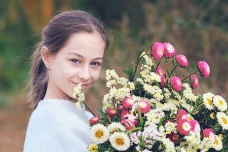 Happy teenage girl in a forest glade holding a huge bright bouquet of flowers in her hands.の写真素材