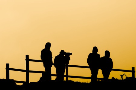 four friends looking through a telescope in a lookout point at sunsetの写真素材