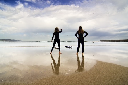 two surfers girls walking on the beach sand to the seaの写真素材