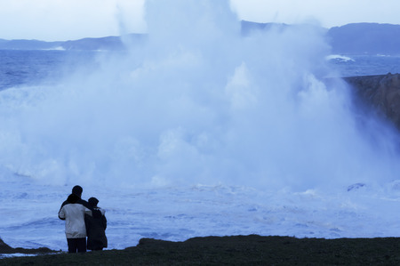 couple look at dusk giant waves in sea storm in Corunna  Spainの写真素材