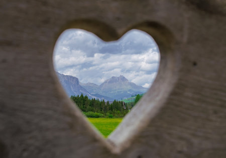 Heart shaped window in the middle of a field with mountains in the backgroundの写真素材
