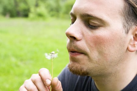 Young man blowing dandelion against green backgroundの写真素材