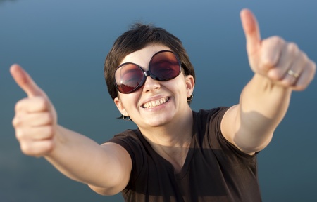 Young brunette girl with big funny sunglasses making thumbs up gesture の写真素材