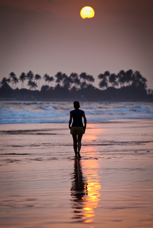 Woman walking on beach at sunsetの写真素材