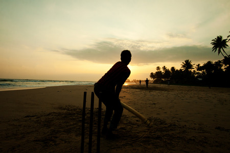 Boy playing cricket at sunset on tropical beach in Sri Lanka