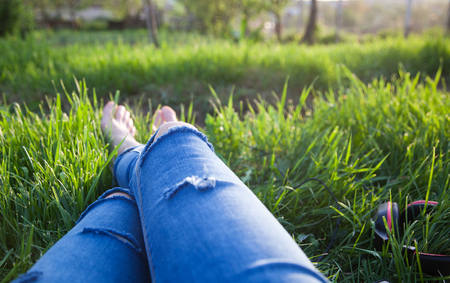 legs of hipster woman wearing torn jeans lying in green grass with smartphone and headsets enjoying sunset - summertime relaxationの写真素材