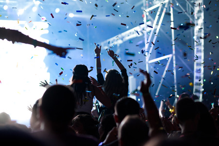 cheering crowd with raised hands and falling confetti at concert - music festivalの写真素材