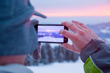 Man taking picture of sunrise over snow covered fir treesの写真素材