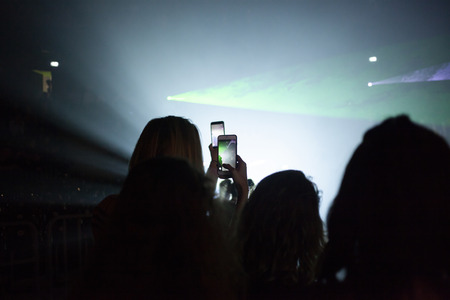 woman taking pictures or filming at an event with a smartphone against green neon lights