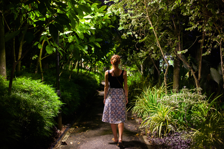 woman walking in a park with tropical trees at nightの写真素材