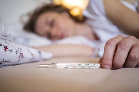 woman  in bed with fever focus on thermometer coronavirus or COVID-19 sympthoms