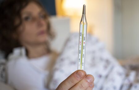 woman  in bed with fever focus on thermometer coronavirus or COVID-19 sympthoms