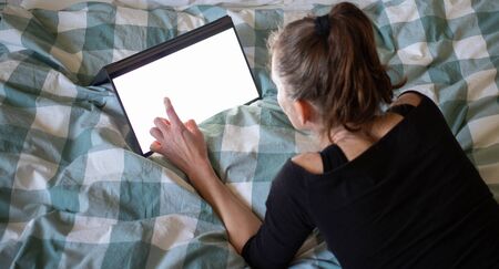 woman using laptop or tablet in bed white empty screen for copy spaceの写真素材