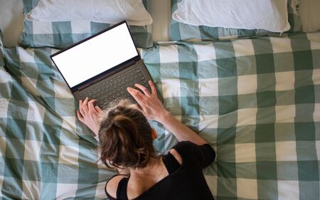 woman using laptop or tablet in bed white empty screen for copy spaceの写真素材