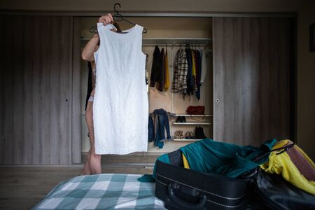 woman packing a suitcase trying on clothes wardrobe in background