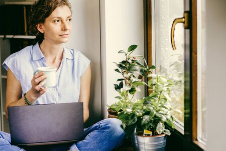 pensive woman working from home looking out on window thinking about future, relationship, career